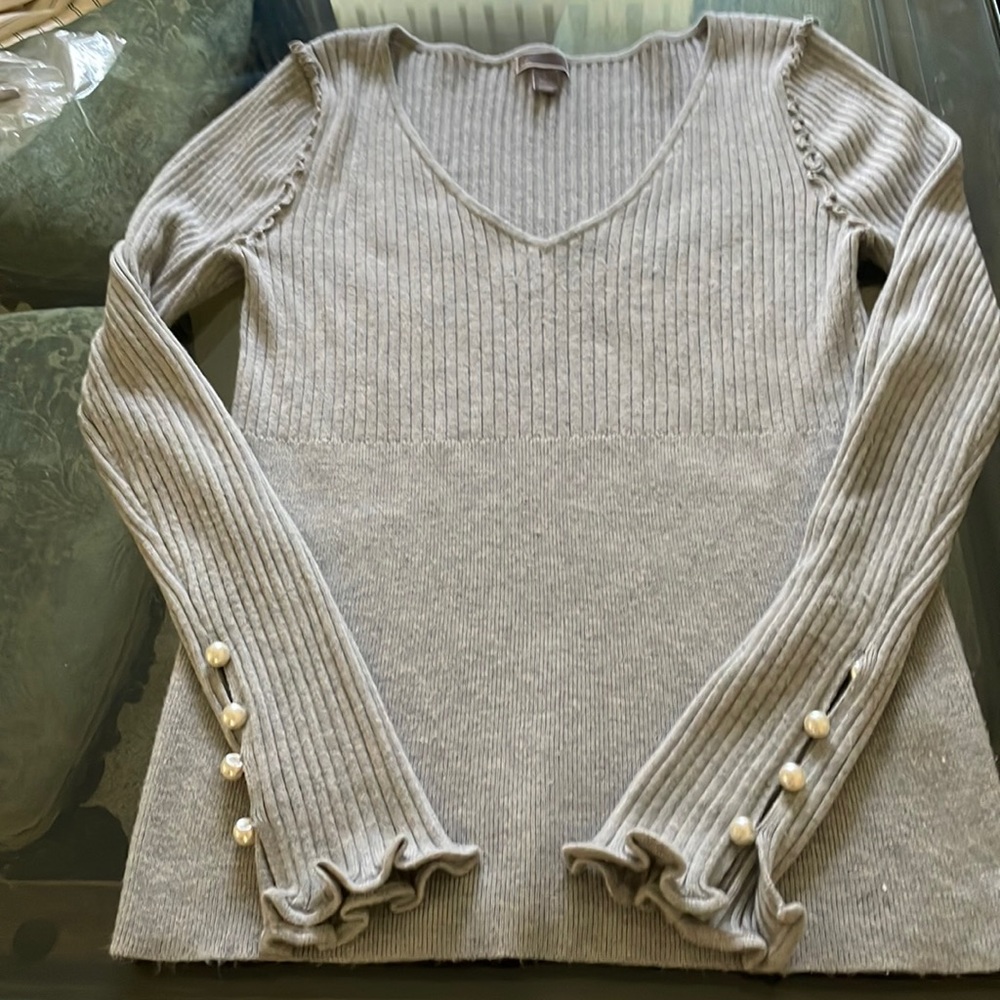 A gray sweater with a lot of detail on the shoulder and pearls on the sleeve.
